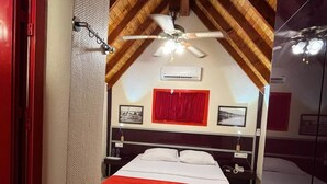 A bedroom with a sloped ceiling, a bed with white bedding and a red accent, a ceiling fan, and a red door. - Seal beach (Mordoğan)