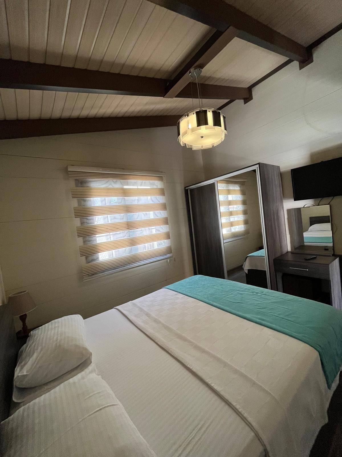 Een hotelkamer met een bed, een nachtkastje, een spiegel en een hanglamp.