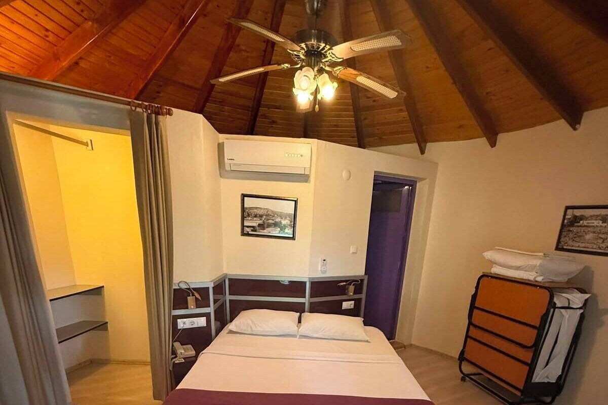 Un dormitorio con cama, ventilador de techo, equipo de aire acondicionado, una puerta y una pequeña mesa con una silla.