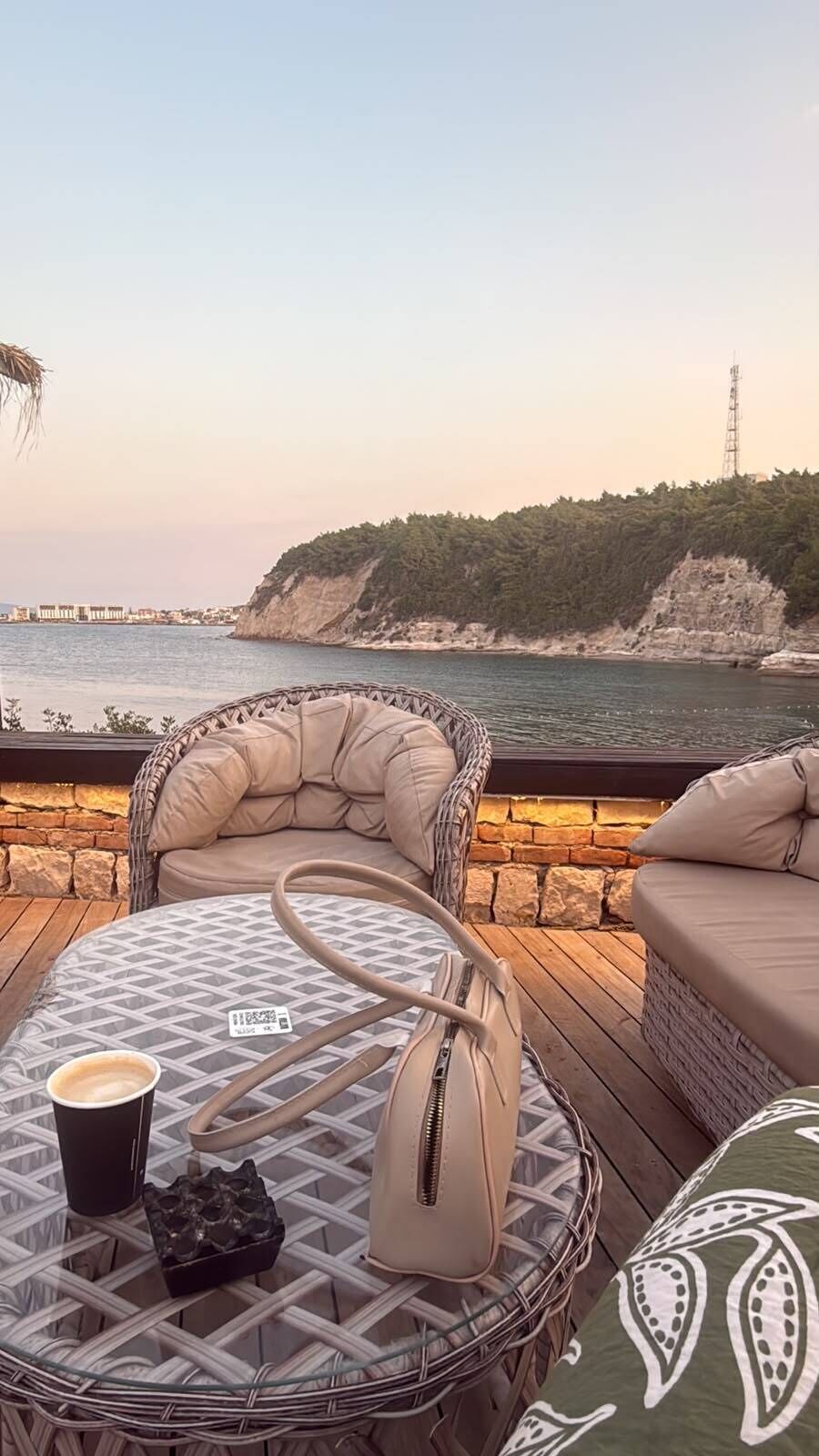 A deck with wicker furniture, a round table with a patterned tablecloth, and a view of the sea and cliffs.