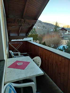 Een balkon met een tafel en stoelen, een houten leuning en uitzicht op een bergachtig landschap.