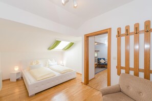 Een slaapkamer met een bed, nachtkastje en een houten scheidingswand met haken.