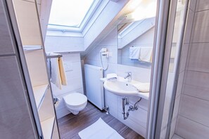 Een compacte, moderne badkamer met dakraam, toilet, wastafel en douche.
