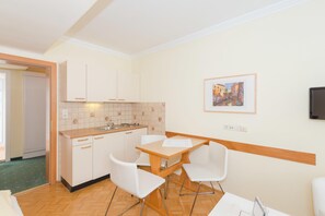 Een compacte keuken met witte kastjes, een houten aanrechtblad en een eethoek met witte stoelen.