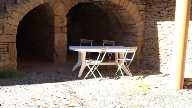 An outdoor stone archway leading to a covered patio area with a table and chairs.