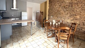 A kitchen with a dining area, featuring a stone wall, tiled flooring, and wooden furniture.