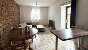 A room with a stone wall, a round wooden table with chairs, a sofa, a TV, and a window with curtains.