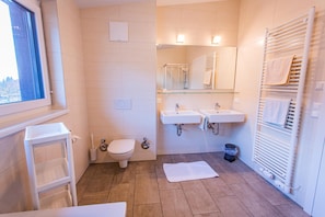Ein Badezimmer mit Toilette, zwei Waschbecken, einer Glasablage, einem Handtuchhalter und einem Fenster.
