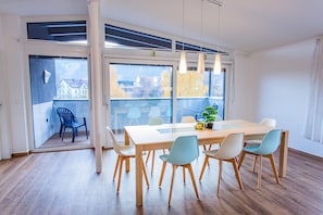 Ein moderner Essbereich mit großem Tisch, Stühlen und Blick durch hohe Fenster.