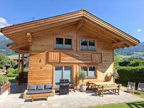 Eine Holzhütte mit Balkon und Grill, mit einem Schild mit der Aufschrift 'CHALET-HUBER'.