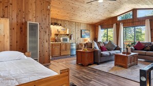 Interior de una cabaña de madera con cama, sofá y comedor.