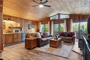 L’intérieur d’un chalet en bois comprend une cuisine, deux canapés, une table à manger et de grandes fenêtres.