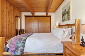 Una stanza in legno con un letto, una testiera in legno, un quadro al muro e un piccolo tavolo con una bottiglia.