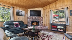 Un interior de cabaña acogedor, con chimenea, sofá de cuero y televisión.