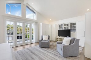 Ein geräumiger Wohnbereich mit einem großen Fernseher, zwei grauen Sofas und einem Balkon mit Glastüren.