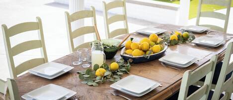 Mesa de comedor dispuesta para seis personas, con platos blancos, un cuenco de limones y una jarrón de limonada.