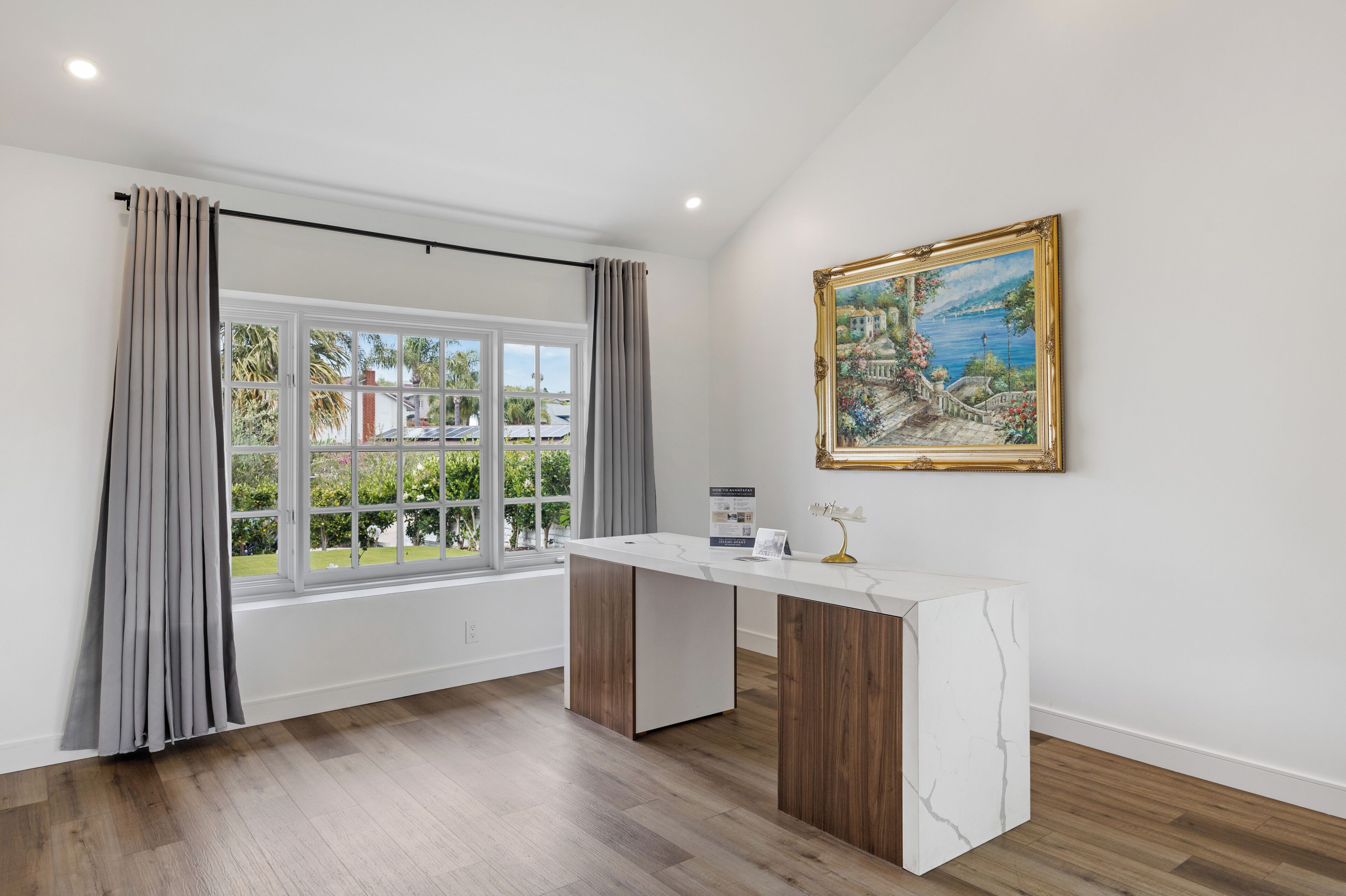A room with a large window, a marble counter, and a framed painting on the wall.