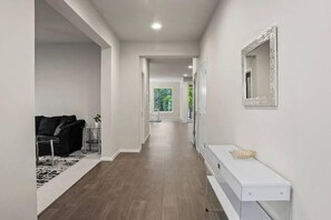 Un couloir avec une console blanche, un miroir et un canapé noir.