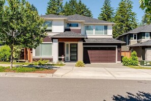 Une maison moderne à deux étages, dotée d’un garage, d’un porche et d’une pelouse bien entretenue.