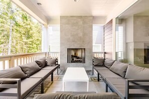 Un salon moderne doté d’une cheminée, de bancs intégrés et d’une grande fenêtre donnant sur une forêt.