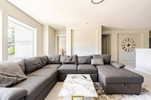 A modern living room with a sectional sofa, a marble coffee table, and a large wall clock.