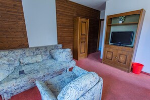 Ein Wohnzimmer mit einer Couch, einem Fernseher auf einem Holzschrank und einem roten Teppich.