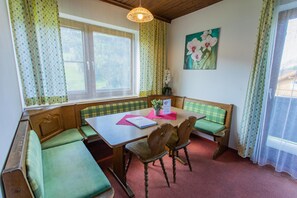 Ein Zimmer mit einer Sitzecke mit Holzbank, einem Tisch und einem Fenster mit Vorhängen.