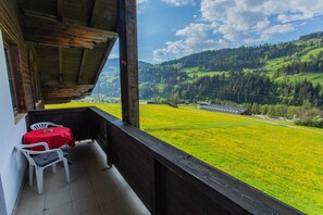 Een balkon met een rode tafel en stoelen, met uitzicht op een groene vallei met gebouwen.