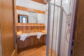 Een badkamer met een houten wastafelmeubel, twee wastafels, een spiegel en een douchecabine met glazen wanden.