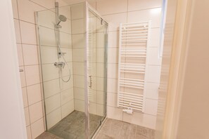 Eine Duschkabine mit Glas, einer Handbrause, einer Glastür und einem weißen Handtuchhalter.