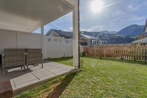 Ein überdachter Patio-Bereich mit Gartenmöbeln, einem Holzzaun und Blick auf eine gebirgige Landschaft.