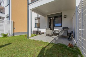 Eine moderne Terrassenanlage mit Tisch und Stühlen, einer Schiebetür und einem kleinen Gartenbereich.