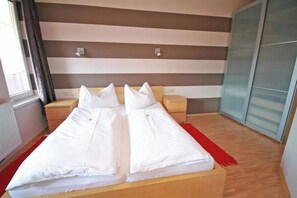 Ein Doppelbett mit weißer Bettwäsche, zwei Nachttische, ein roter Teppich und ein Fenster mit Vorhängen.