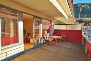 Ein Balkon mit Holztisch und -stühlen, einer roten Wand und Blick auf die umliegende Landschaft.