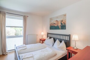 Ein Hotelzimmer mit einem Bett, zwei Nachttischen, einem fensterbelaubten Fenster, einer Heizung und einem Bild an der Wand.