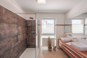Ein modernes Badezimmer mit begehbarer Dusche, zwei Waschbecken, einem großen Spiegel und einer Topfpflanze.