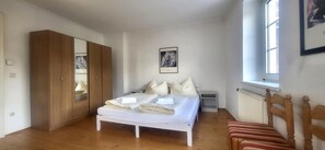 Ein Schlafzimmer mit Bett, Holzschrank, Heizkörper und Fenster.