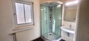 Ein Badezimmer mit Duschkabine, Fenster, Waschbecken und Spiegel.