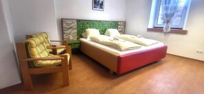 Ein Schlafzimmer mit Bett, Stuhl, Fenster und einem Wandbild.