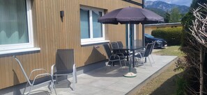 Eine Terrasse mit Tisch und Stühlen, ein Fenster und Blick auf Berge.