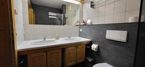 Ein modernes Badezimmer mit zwei Waschbecken, Holzschränken, einem Spiegel und einer Toilette.