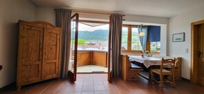 Ein Zimmer mit Holzschrank, Tisch mit Bank und Blick auf eine gebirgige Landschaft durch große Fenster.