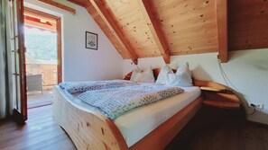 Ein Schlafzimmer mit Holzbalkendecke, einem Bett mit gemusterten Betttextilien und Blick ins Freie.