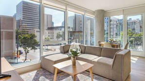Uma sala de estar moderna com um sofá, uma mesa de centro e vista para o horizonte urbano através de grandes janelas.