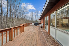 A wooden deck with outdoor seating, a barbecue grill, and a view of trees and hills.