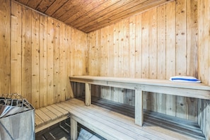A wooden sauna room with benches and a metal container.