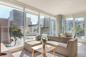 Ein modernes Wohnzimmer mit einer Couch, einem Couchtisch und Blick auf die Skyline durch große Fenster.