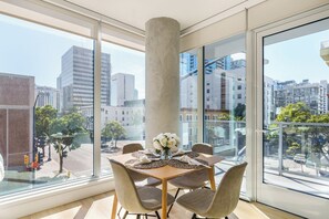 Ein Essbereich mit großem Fenster, einem Tisch mit weißen Blumen und Blick auf die Stadtlandschaft.