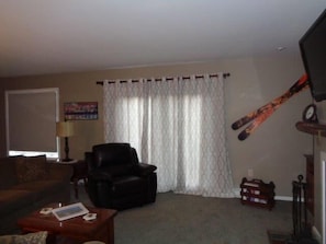 Ein Wohnzimmer mit einer Couch, einem Ledersessel, einem Couchtisch, einem Fernseher und einem Skiständer.