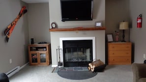 Ein Wohnzimmer mit Kamin, einem darüber montierten Fernseher, einem Holzschrank und einem Feuerlöscher an der Wand.